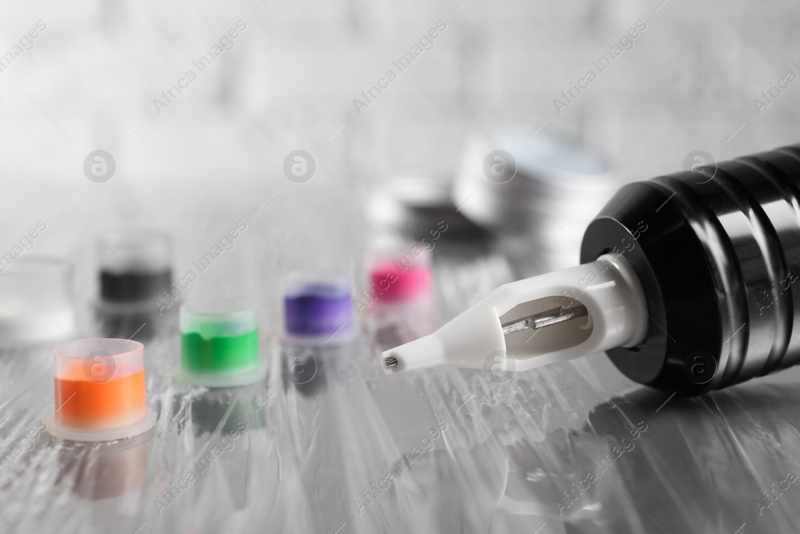 Photo of Modern professional tattoo machine and caps with colorful inks on table, closeup