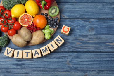 Photo of Cubes with phrase VITAMIN C and fresh products on blue wooden table, flat lay. Space for text