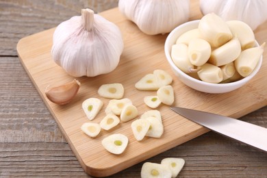 Photo of Aromatic cut garlic, cloves and bulbs on wooden table, closeup