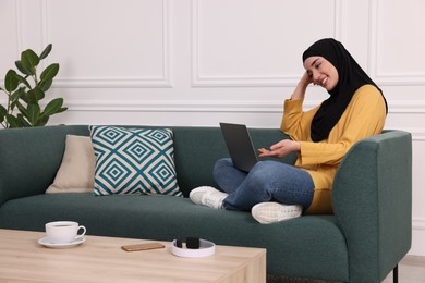 Muslim woman in hijab using video chat on laptop indoors. Space for text