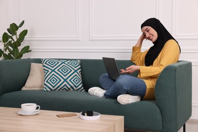 Photo of Muslim woman in hijab using video chat on laptop indoors. Space for text