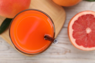 Photo of Tasty grapefruit juice in glass and fresh fruits on light wooden table, flat lay