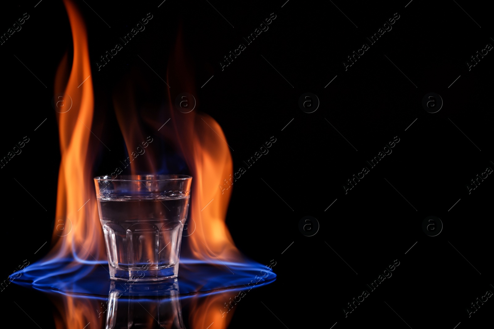 Photo of Vodka in glass and flame on black background, space for text