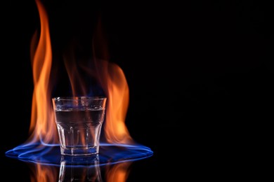 Photo of Vodka in glass and flame on black background, space for text
