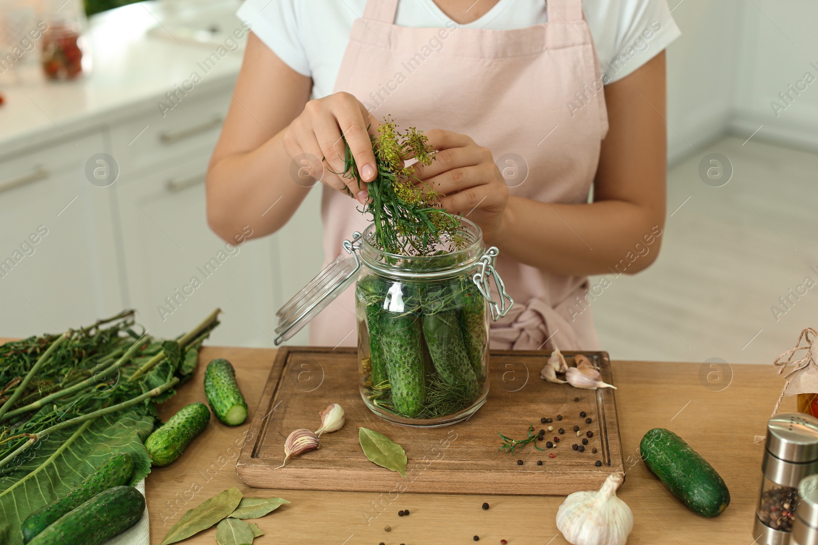 Photo of Woman putting dill into pickling jar at table in kitchen, closeup