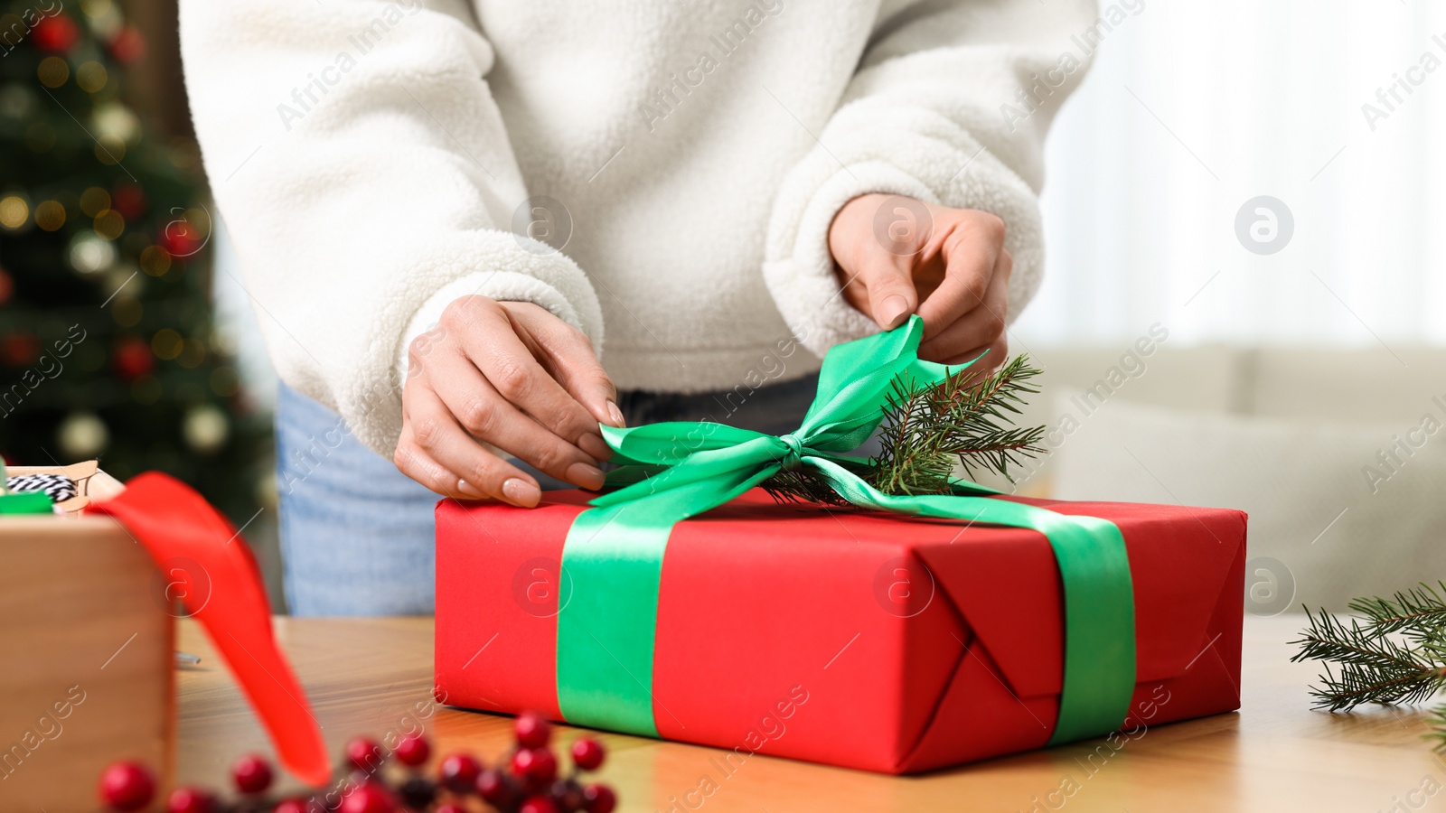 Photo of Woman wrapping Christmas gift at wooden table indoors, closeup