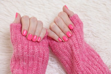 Woman showing her manicured hands with pink nail polish on faux fur mat, closeup