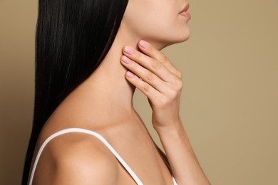 Photo of Young woman doing thyroid self examination on beige background, closeup