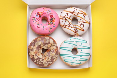 Photo of Box with tasty glazed donuts on yellow background, top view