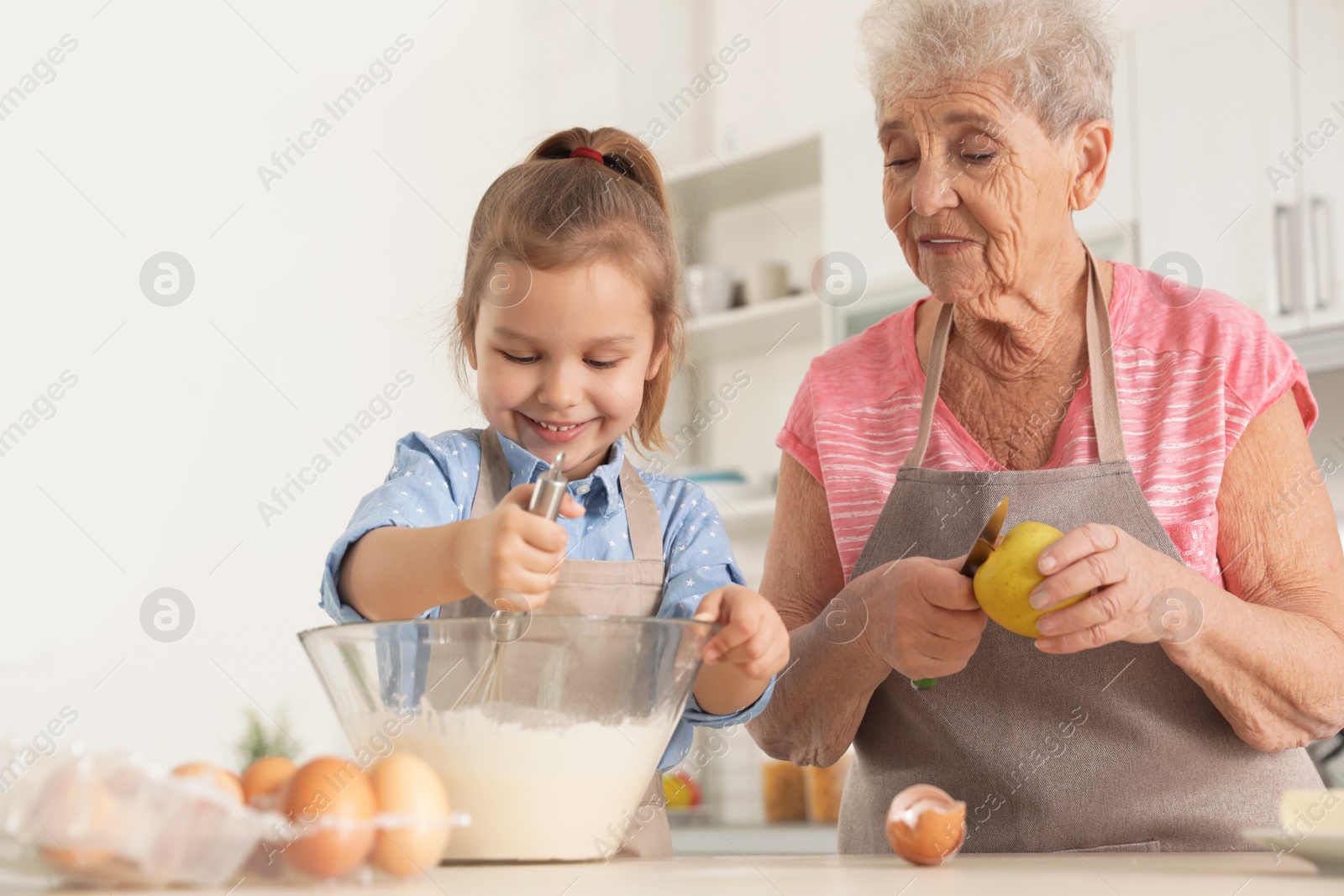 Photo of Cute girl and her grandmother cooking in kitchen