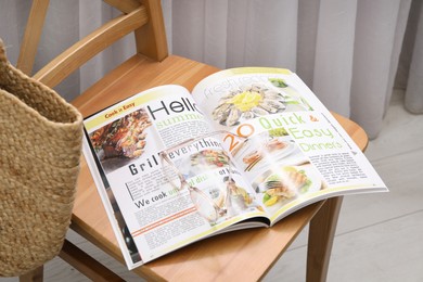 Photo of Open  healthy food magazine and wicker bag on wooden chair indoors