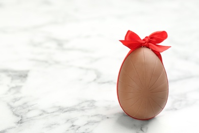 Photo of Sweet chocolate egg with red bow on white marble table. Space for text