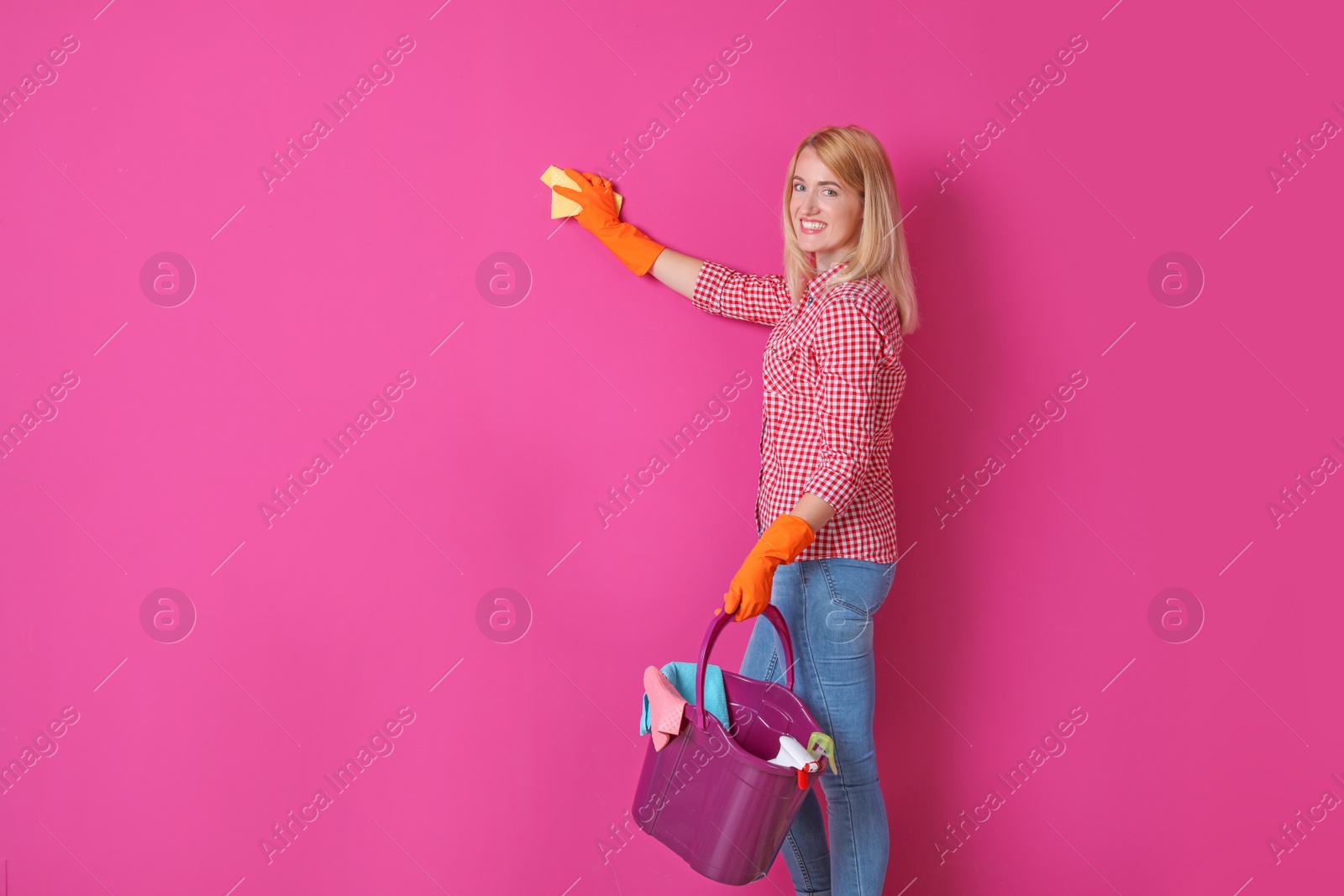 Photo of Woman in gloves cleaning color wall with rag