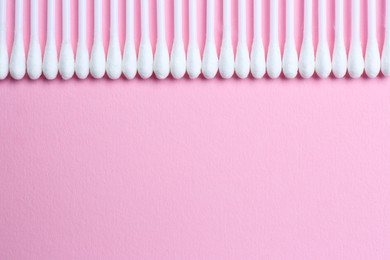 Many cotton buds on pink background, flat lay. Space for text