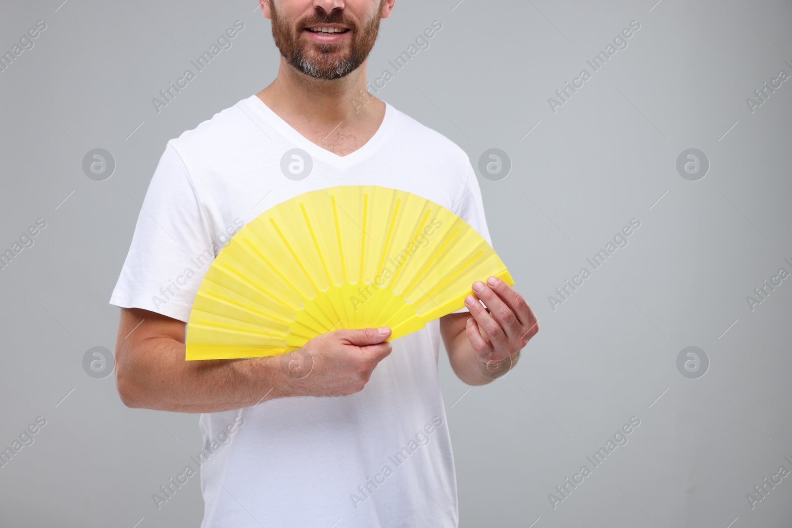 Photo of Man holding hand fan on light grey background, closeup. Space for text