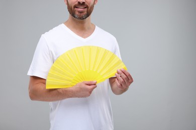 Man holding hand fan on light grey background, closeup. Space for text