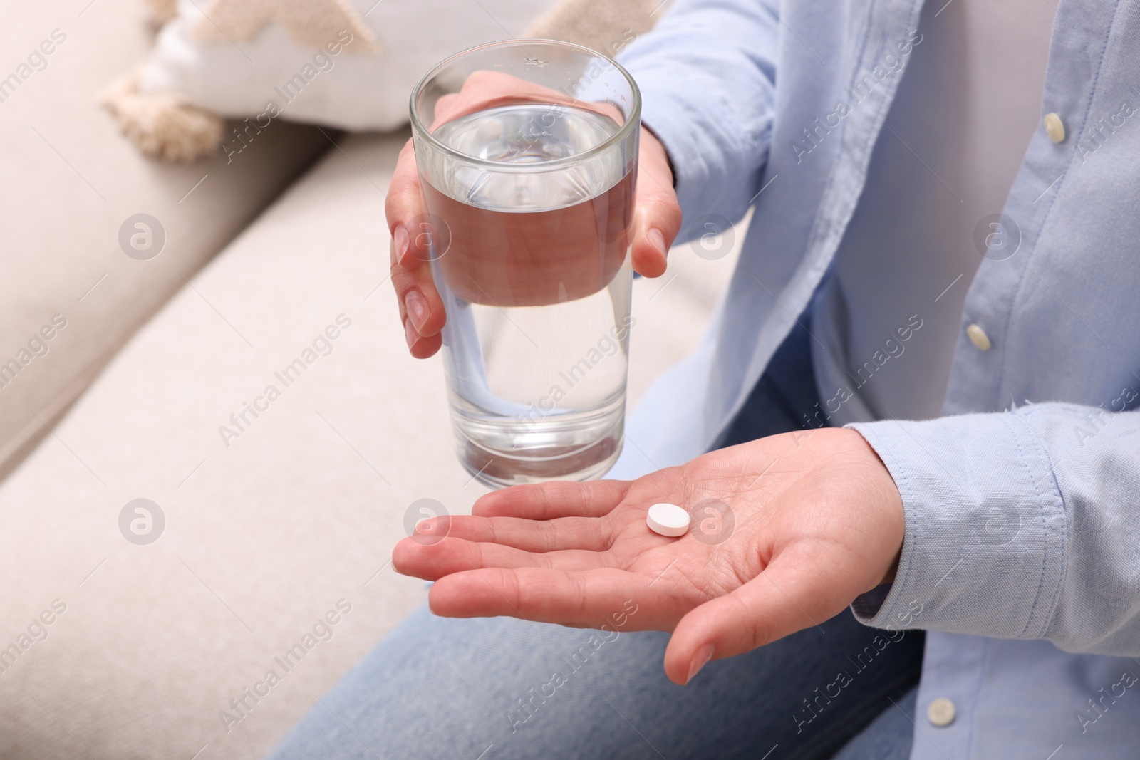 Photo of Woman with glass of water and pill on sofa, closeup