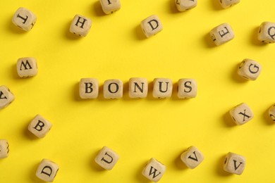 Image of Word Bonus made of wooden cubes with letters on yellow background, flat lay