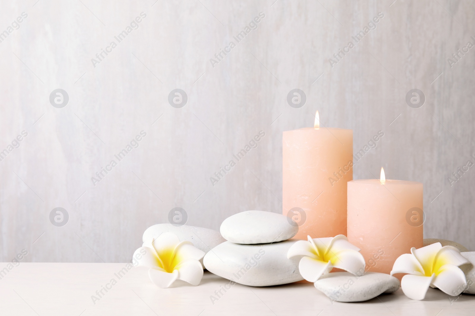 Photo of Zen stones, lighted candles and exotic flowers on table against light background. Space for text