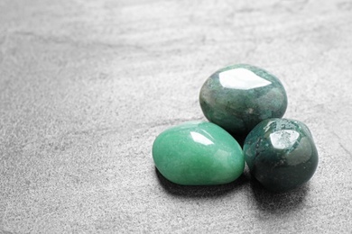 Photo of Beautiful green gemstones on grey table, space for text