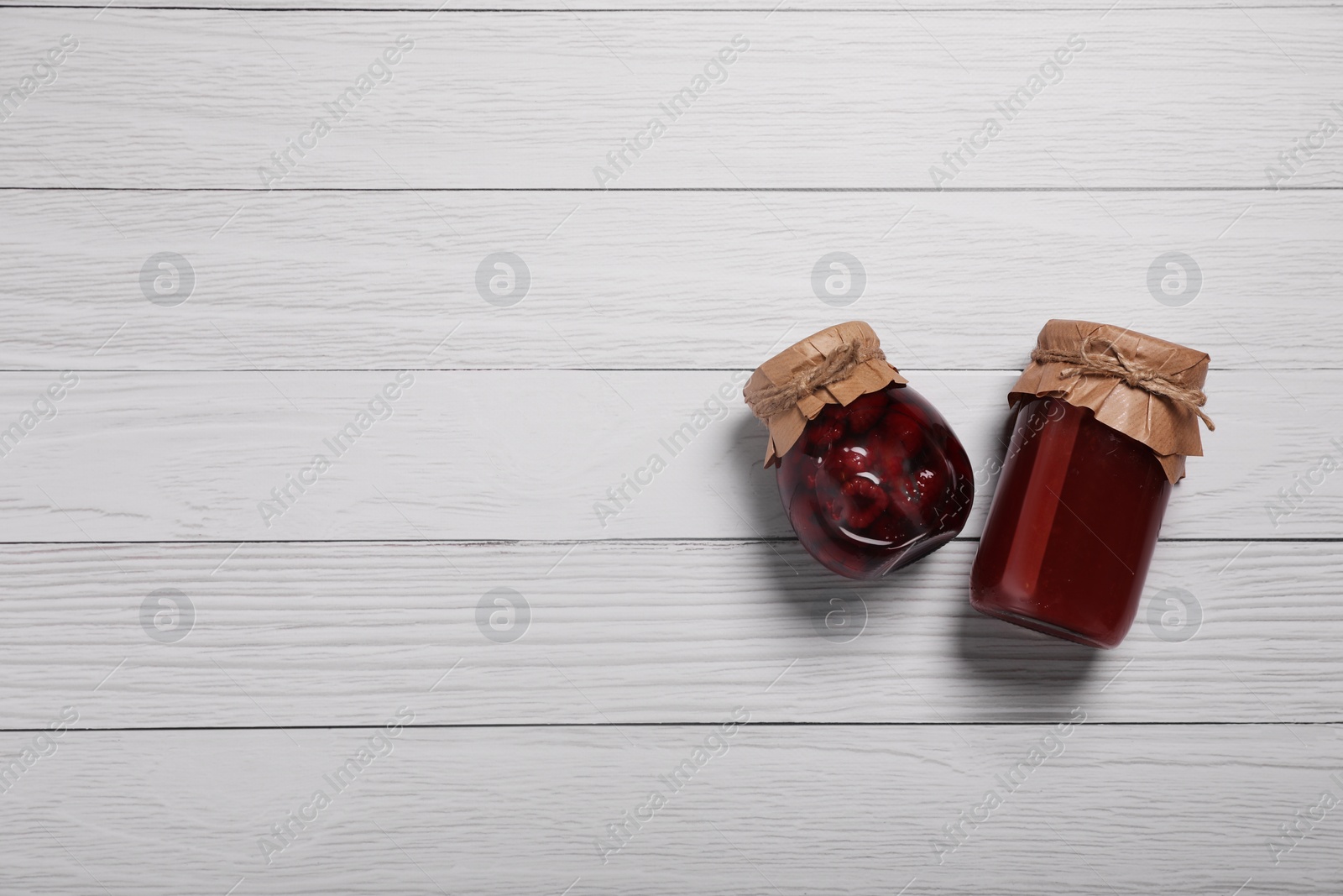 Photo of Jars with preserved fruit jams on white wooden table, flat lay. Space for text