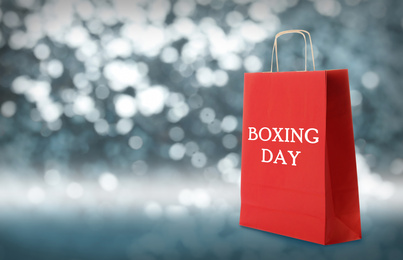 Red shopping bag with text Boxing Day on blurred background, closeup. Space for text