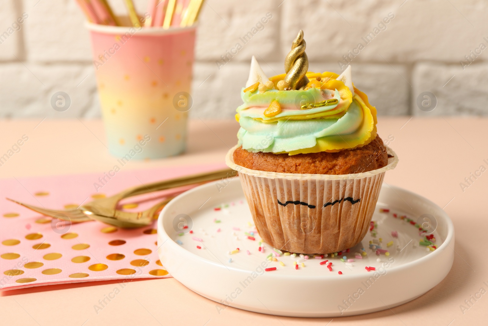 Photo of Plate with cute sweet unicorn cupcake on beige table