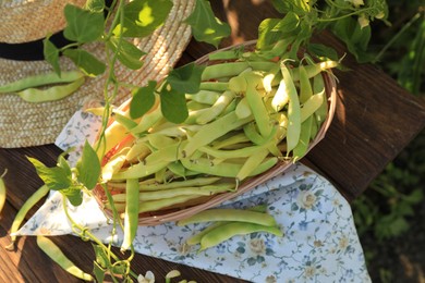 Photo of Wicker basket with fresh green beans on wooden table in garden, top view
