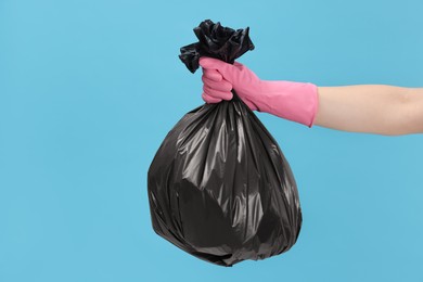 Photo of Woman holding plastic bag full of garbage on light blue background, closeup