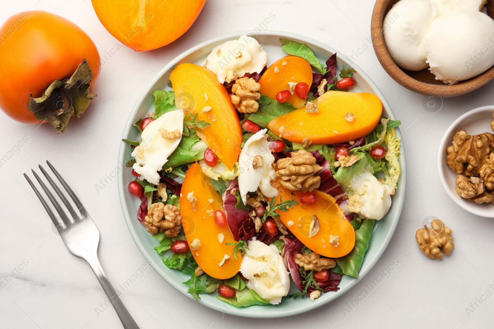 Photo of Delicious persimmon salad with cheese and pomegranate served on white marble table, flat lay