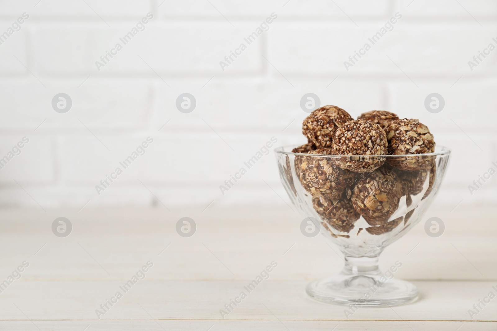 Photo of Glass dessert bowl of tasty chocolate balls on white wooden table, space for text