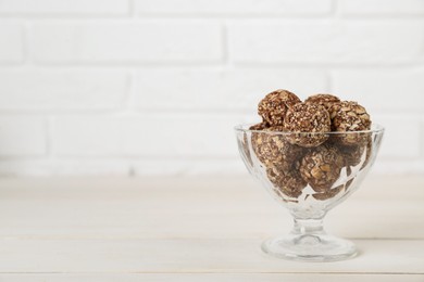 Glass dessert bowl of tasty chocolate balls on white wooden table, space for text