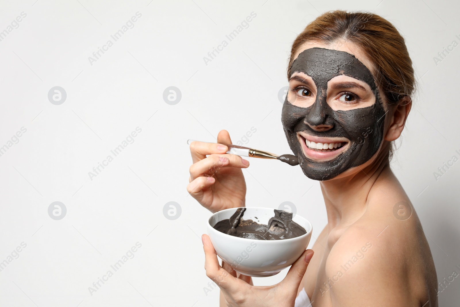 Photo of Beautiful woman applying black mask onto face against light background. Space for text