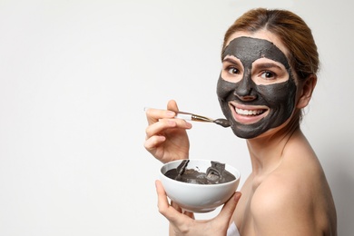 Photo of Beautiful woman applying black mask onto face against light background. Space for text