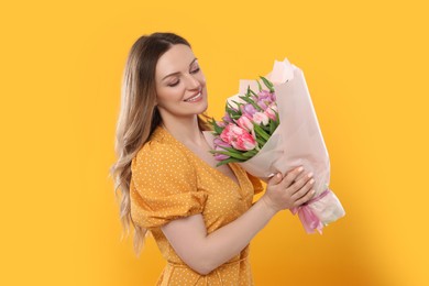 Photo of Happy young woman with bouquet of beautiful tulips on yellow background