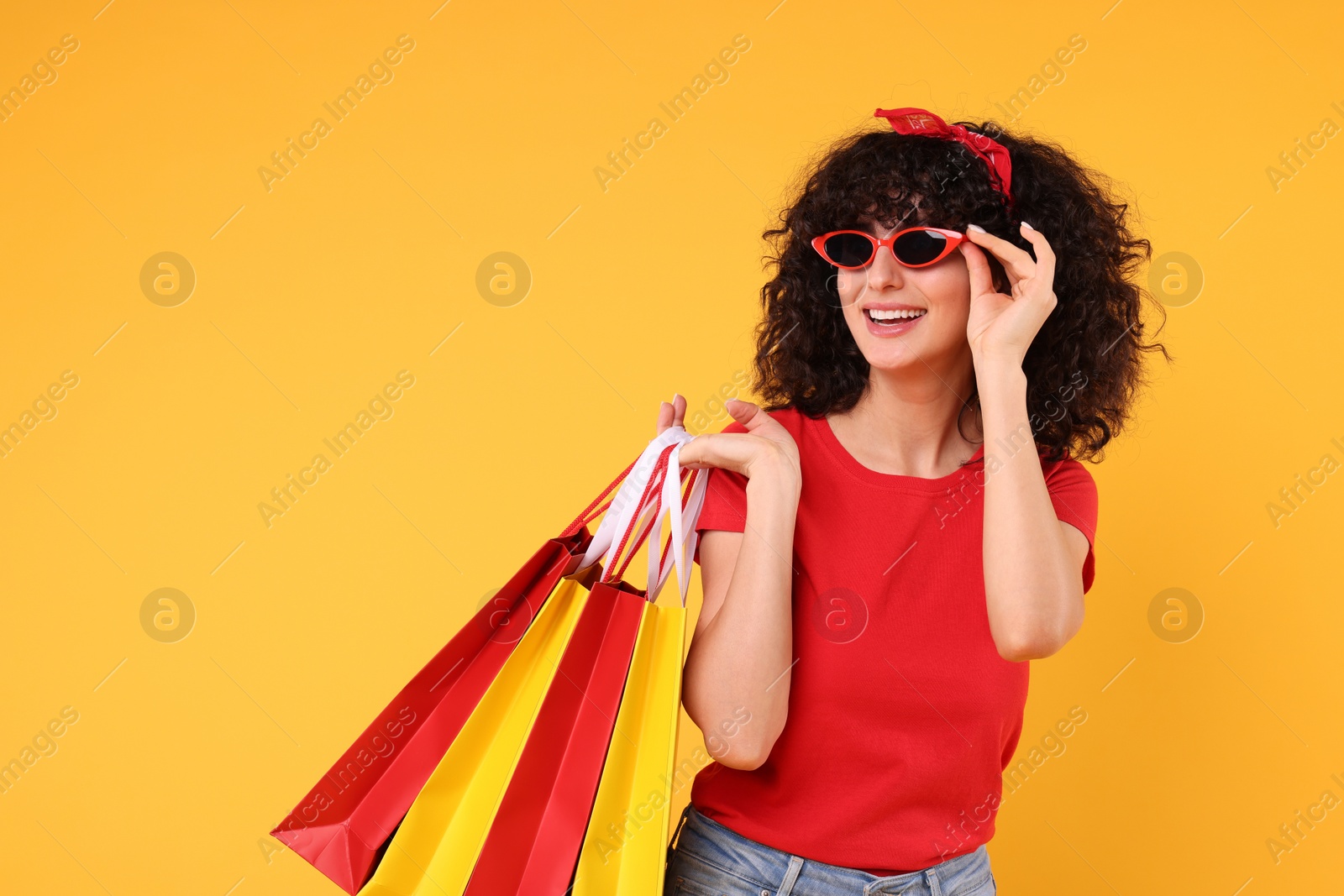 Photo of Happy young woman with shopping bags and stylish sunglasses on yellow background