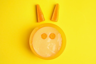 Photo of Baby food in bowl and fresh carrot on yellow background, flat lay