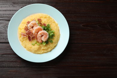 Plate with fresh tasty shrimps, bacon and grits on dark wooden table, top view. Space for text