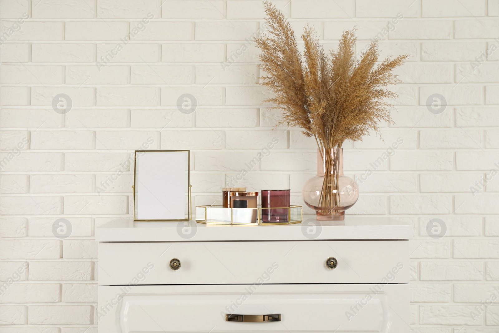 Photo of Modern chest of drawers with decor near white brick wall
