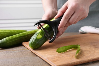 Woman peeling cucumber at wooden table indoors, closeup