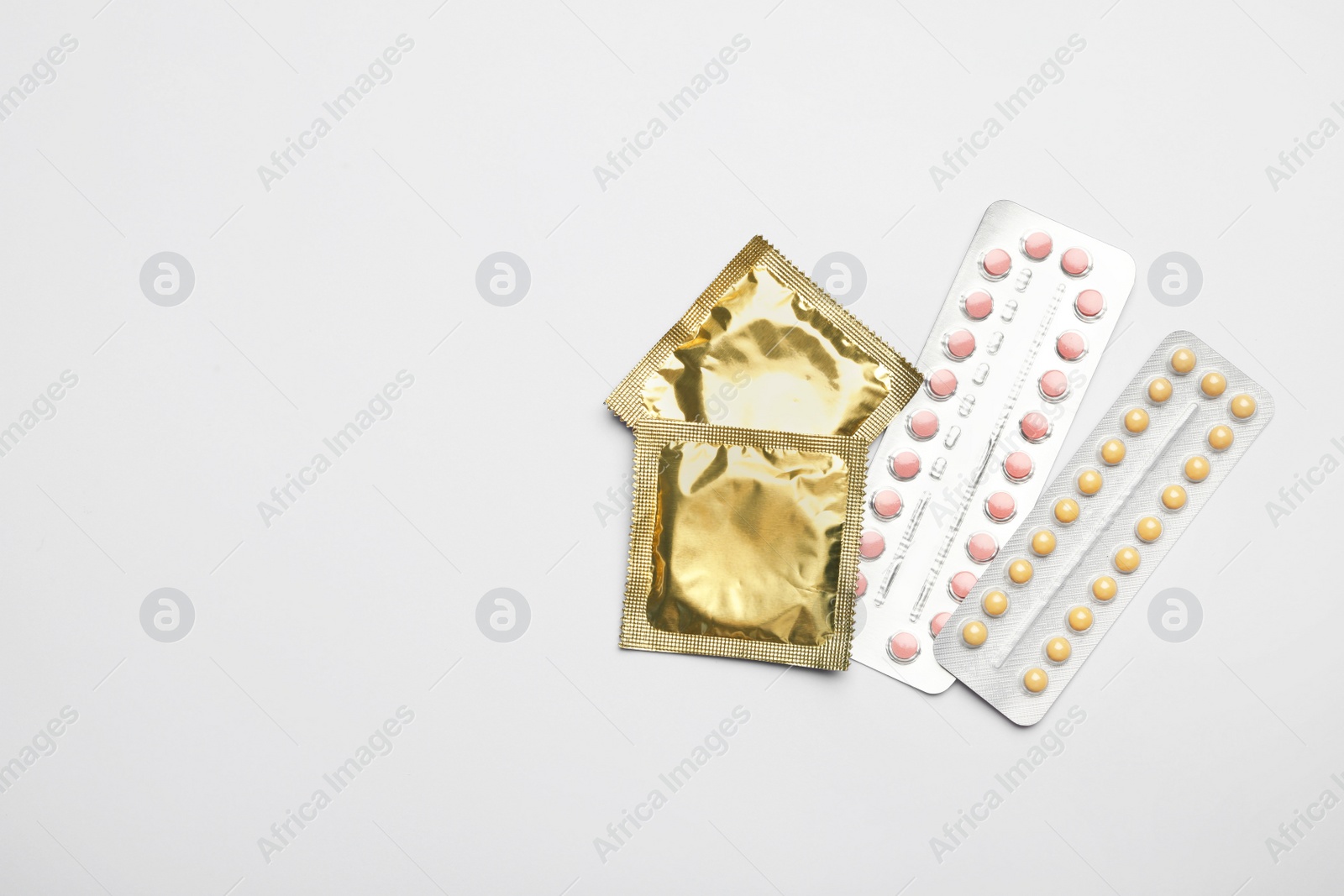 Photo of Condoms and birth control pills on light grey background, flat lay with space for text. Safe sex concept