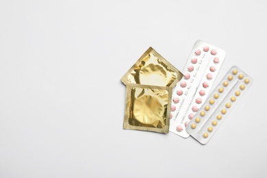 Condoms and birth control pills on light grey background, flat lay with space for text. Safe sex concept