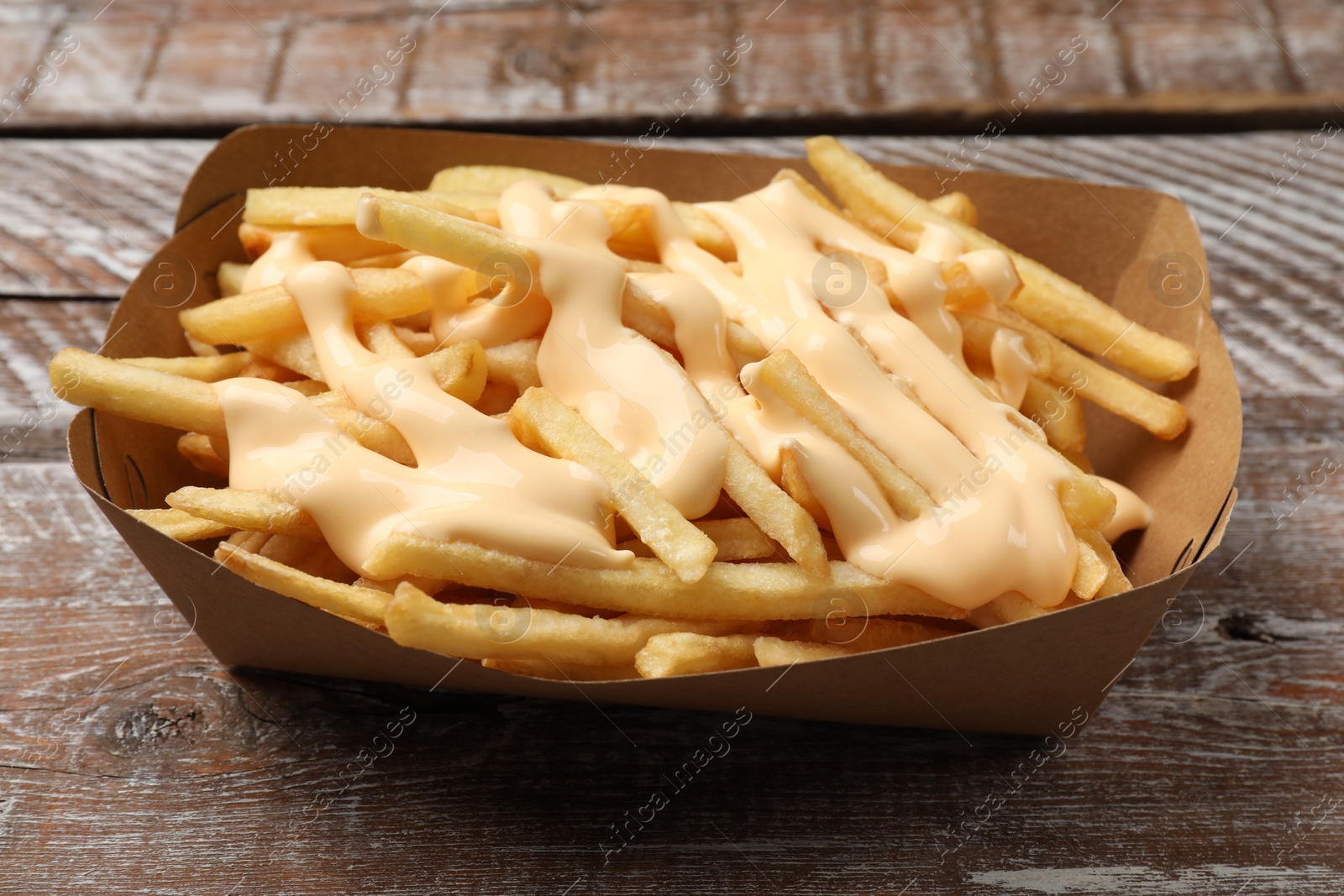 Photo of Delicious French fries with cheese sauce on wooden rustic table, closeup