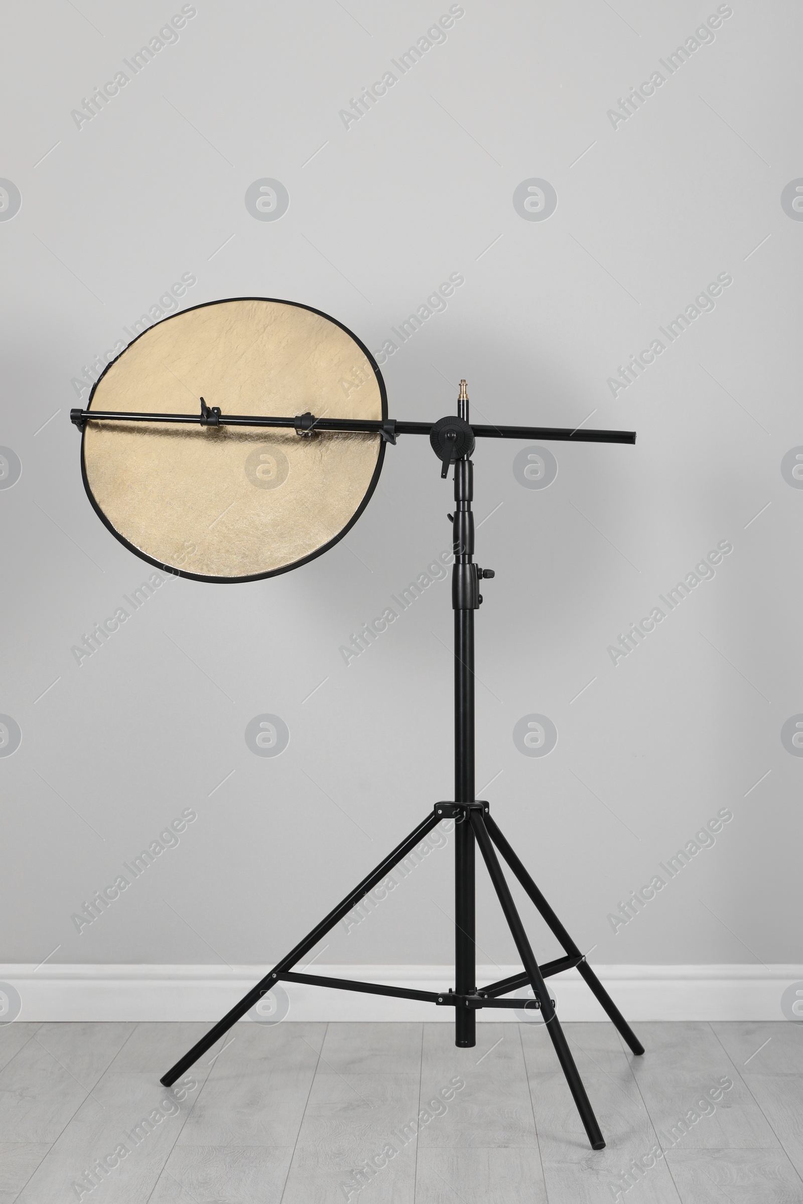 Photo of Studio reflector on tripod near grey wall indoors. Professional photographer's equipment