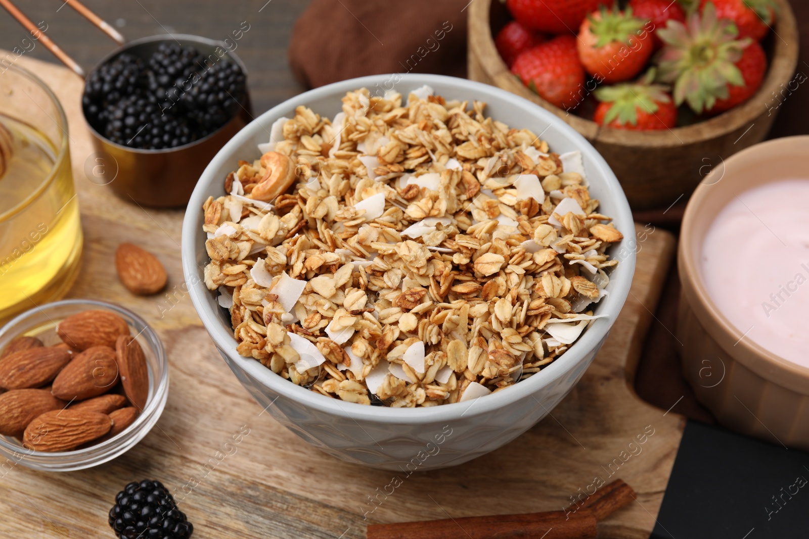 Photo of Tasty granola served with nuts and fresh berries on wooden board, closeup. Healthy breakfast