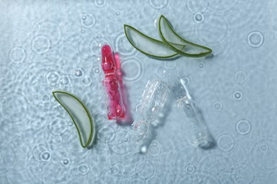 Skincare ampoules with extract of aloe vera and cut leaves in water on light blue background, flat lay