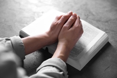 Religion. Christian woman praying over Bible at gray table, closeup