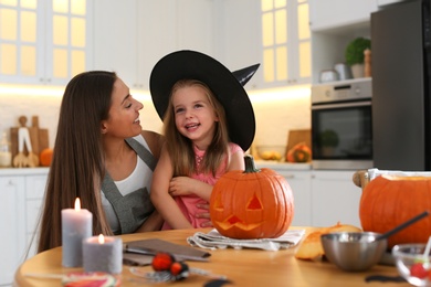 Photo of Mother and daughter with pumpkin jack o'lantern at table in kitchen. Halloween celebration