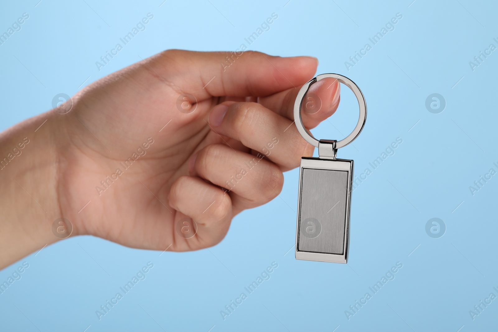 Photo of Woman holding metallic keychain on light blue background, closeup