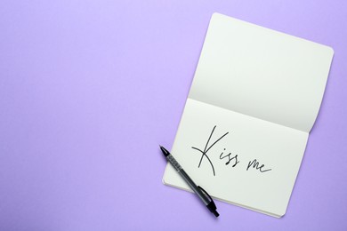 Photo of Open notebook with phrase Kiss Me and pen on violet background, top view. Space for text